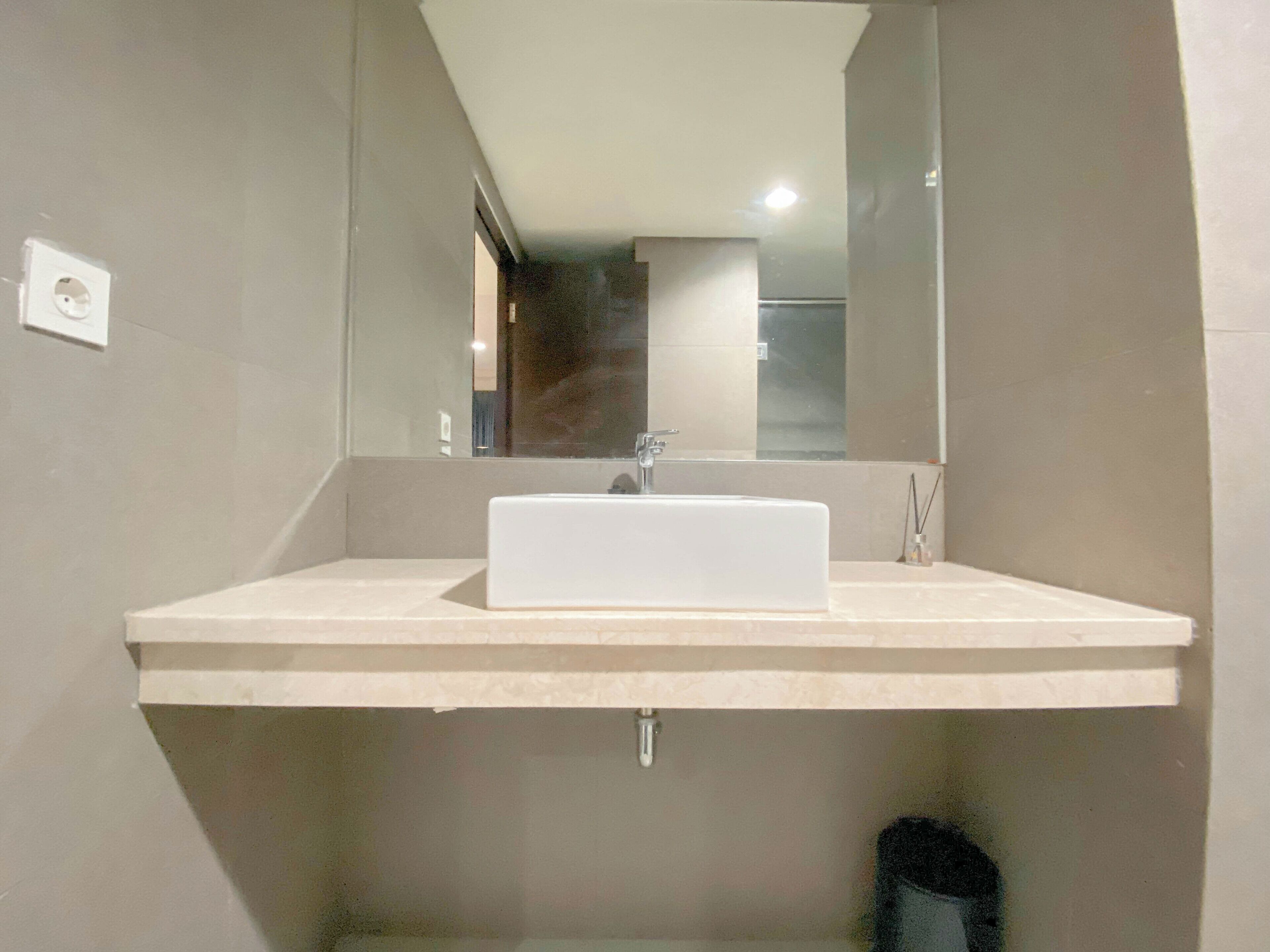 Un baño moderno con un lavamanos rectangular, un espejo y una ducha visible al fondo.