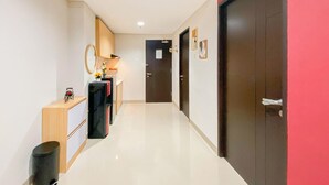 A hallway with a kitchen area, a trash bin, and a door with a handle. - Elegant and Comfortable 1BR at Patraland Amarta Apartment (Ngaglik)