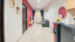 A modern living room with a grey sofa, a small table, and a TV. There is a red cabinet and a mirror on the wall. - Elegant and Comfortable 1BR at Patraland Amarta Apartment (Ngaglik)