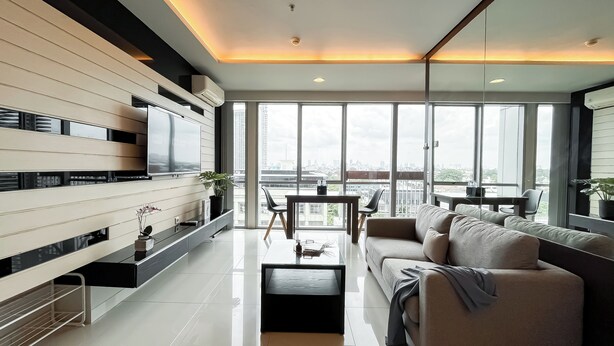 Una sala de estar moderna con un televisor grande, un sofá, una mesa de centro y un balcón con vistas a la ciudad.