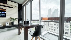 Un espacio de oficina moderno con un amplio ventanal que ofrece vista a la ciudad, un escritorio con una silla, una planta en maceta y un televisor montado.
