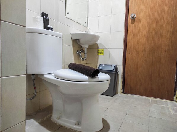 A toilet with a towel on the seat, a trash bin, and a sink.