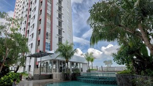 A modern hotel with a swimming pool, surrounded by lush greenery and a tall building in the background. - Luxurious 1BR at Vida View Makassar Apartment (Makassar)