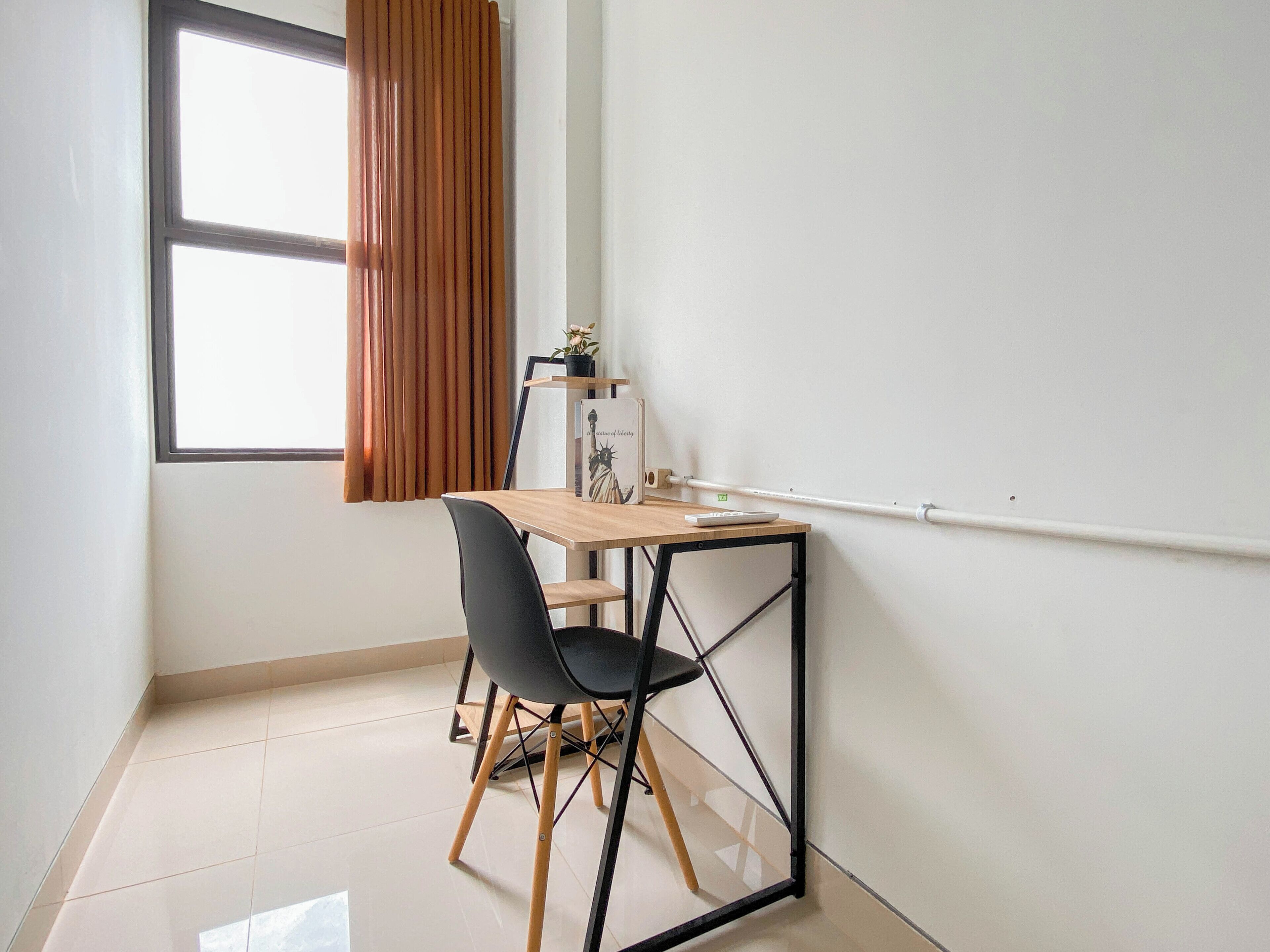 A small, modern room with a desk, chair, and a window with curtains.