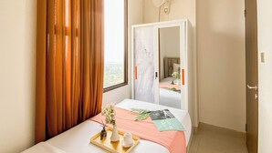 Una camera d'albergo con un letto, un comodino con un vassoio, una finestra con tende, un armadio e un condizionatore d'aria.