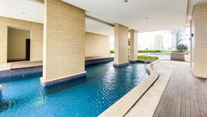 Ein moderner, überdachter Pool mit klarem, blauem Wasser, umgeben von beigefarbenen Säulen und einem Holzboden.