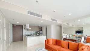 A modern living room with a glass coffee table, an orange sofa, and a kitchen area in the background. - Nice and Comfy 2BR Apartment at Ciputra World 2 (Jakarta)
