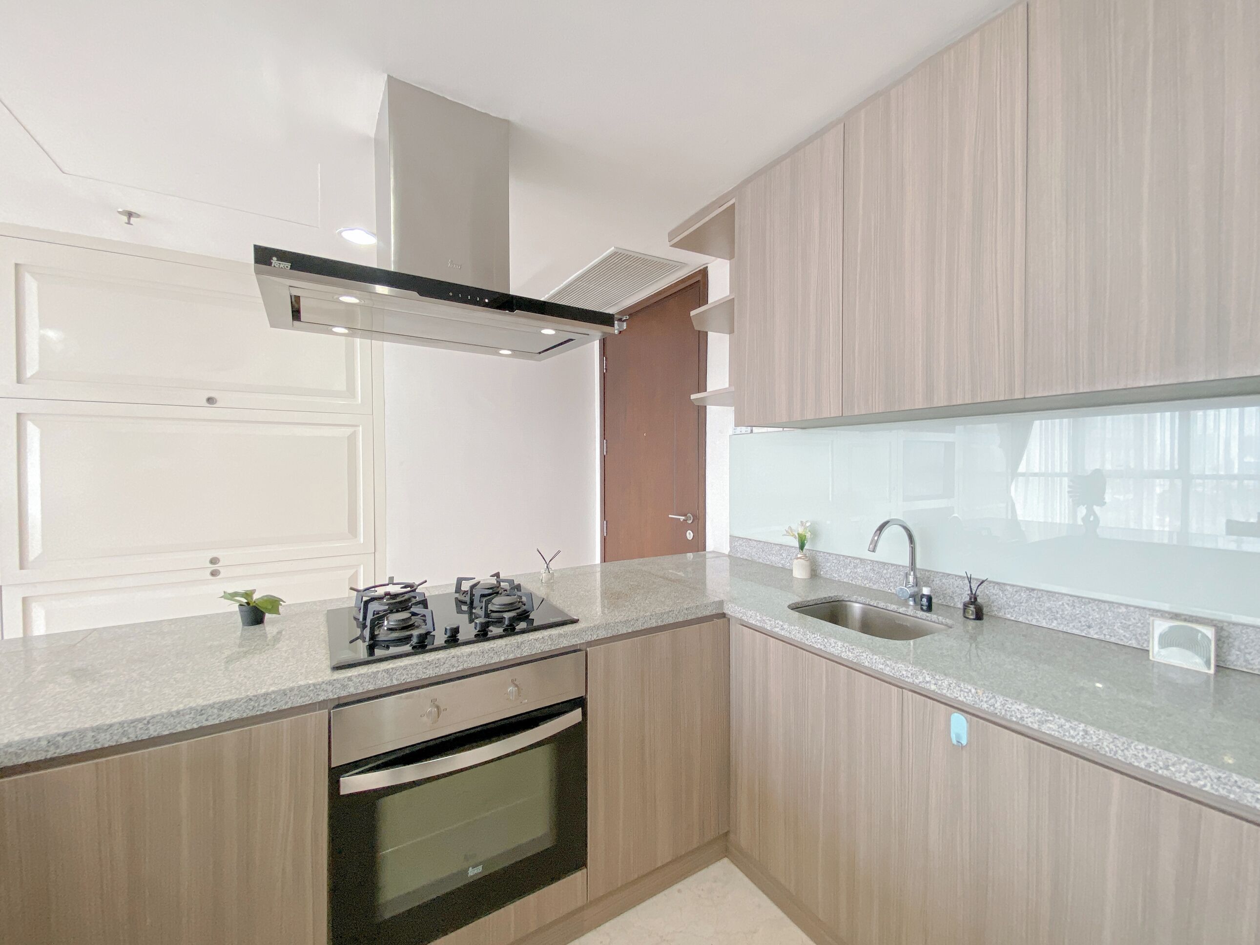 A modern kitchen with a built-in oven, a stainless steel range hood, and a double sink.