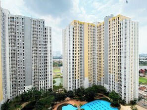 Residents enjoy a modern apartment with a balcony overlooking landscaped grounds and a swimming pool.