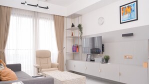 A modern living room with a sofa, armchair, ottoman, TV, and a mounted shelf with decorative items.