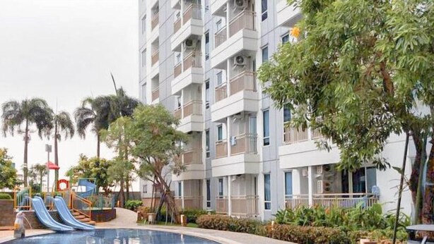 A modern apartment building with balconies, a swimming pool, and a children's play area with slides. - Best View 2BR Apartment Connected to Mall Tanglin Supermall Mansion Apartment (Surabaya)