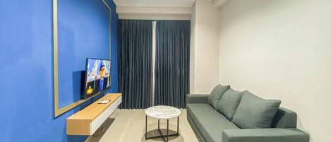 A modern living room with a blue accent wall, a grey sofa, a small round table, and a mounted TV.