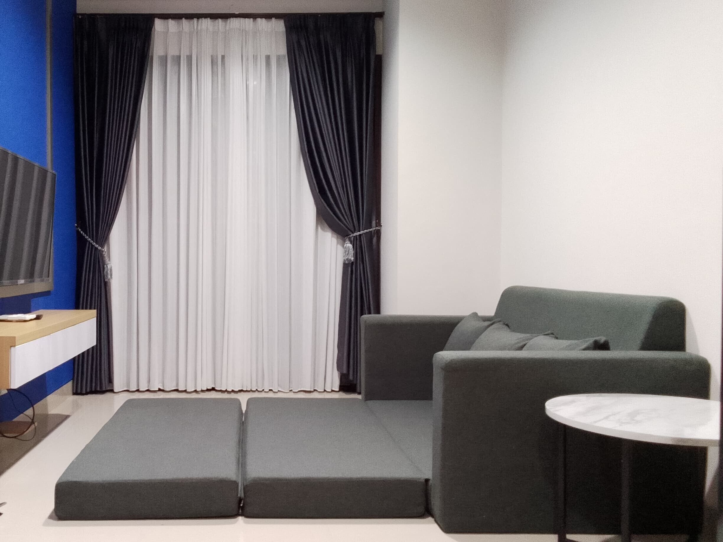 A modern living room with a grey sofa, a small round table, and a TV on a wooden stand.