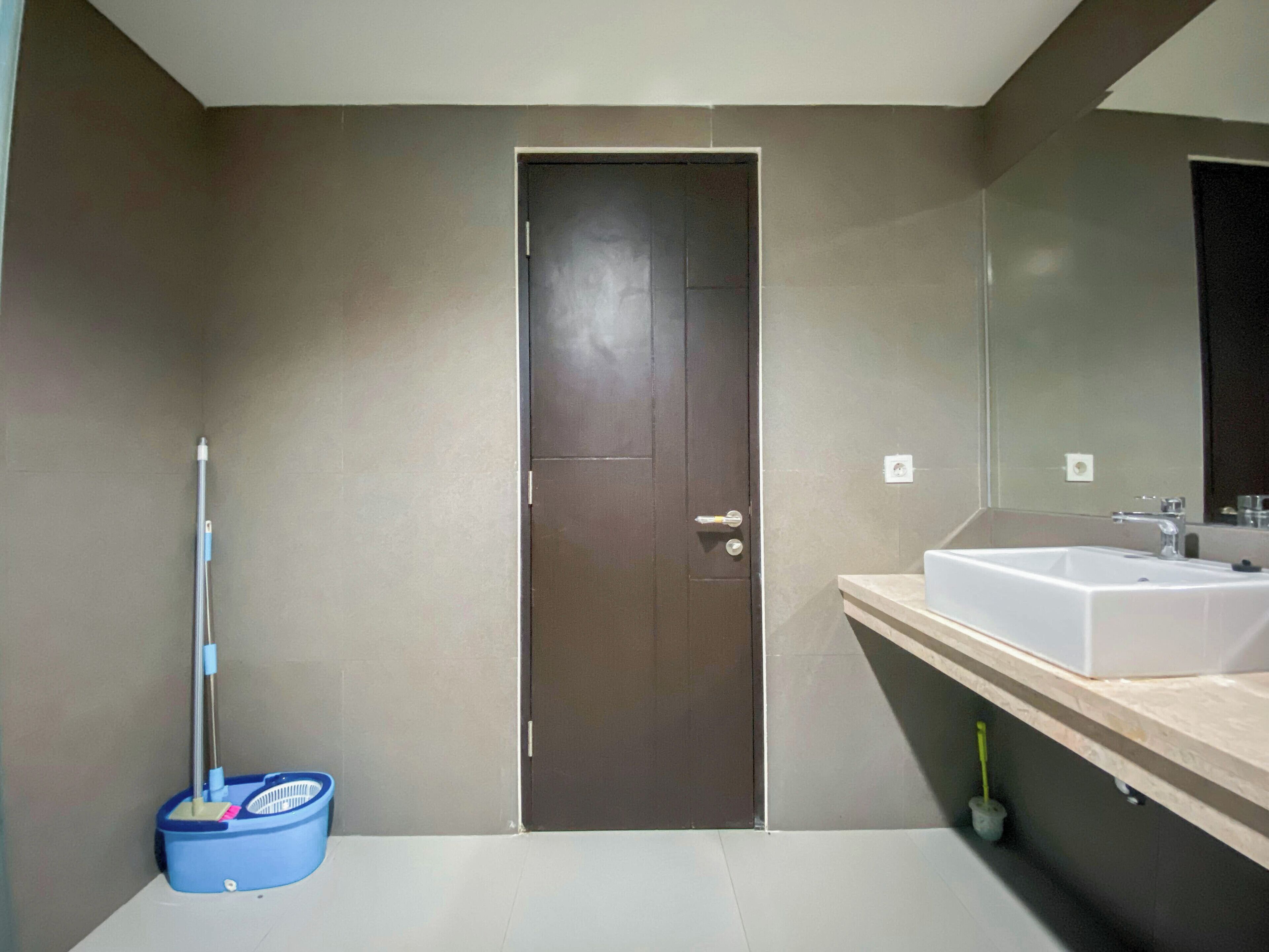 Een badkamer met een donkere deur, een wastafel en een dweil die tegen de muur staat.