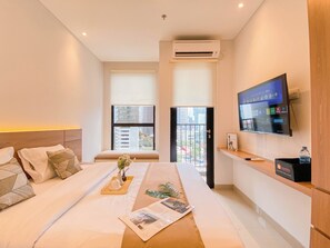 A modern hotel room with a large bed, a TV mounted on the wall, and a balcony with a city view. - Comfy Studio at Ciputra World 2 Apartment (Jakarta)