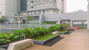 Een modern gebouw met een glazen gevel, een dakterras met plantenbakken en groen, en een overdekt zitgedeelte.