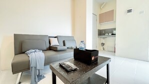 A modern living room with a grey sofa, a small black table with a remote control, and a water bottle. - Good Place 1BR at Menara Kebon Jeruk Apartment (Jakarta)
