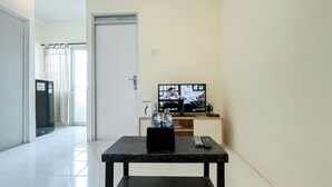 A living room with a television, a small table, and a door leading to another room. - Good Place 1BR at Menara Kebon Jeruk Apartment (Jakarta)