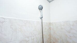 Eine Dusche mit Handbrause und flexiblen Schlauch, an einer Wand mit weißen Marmorfliesen befestigt.