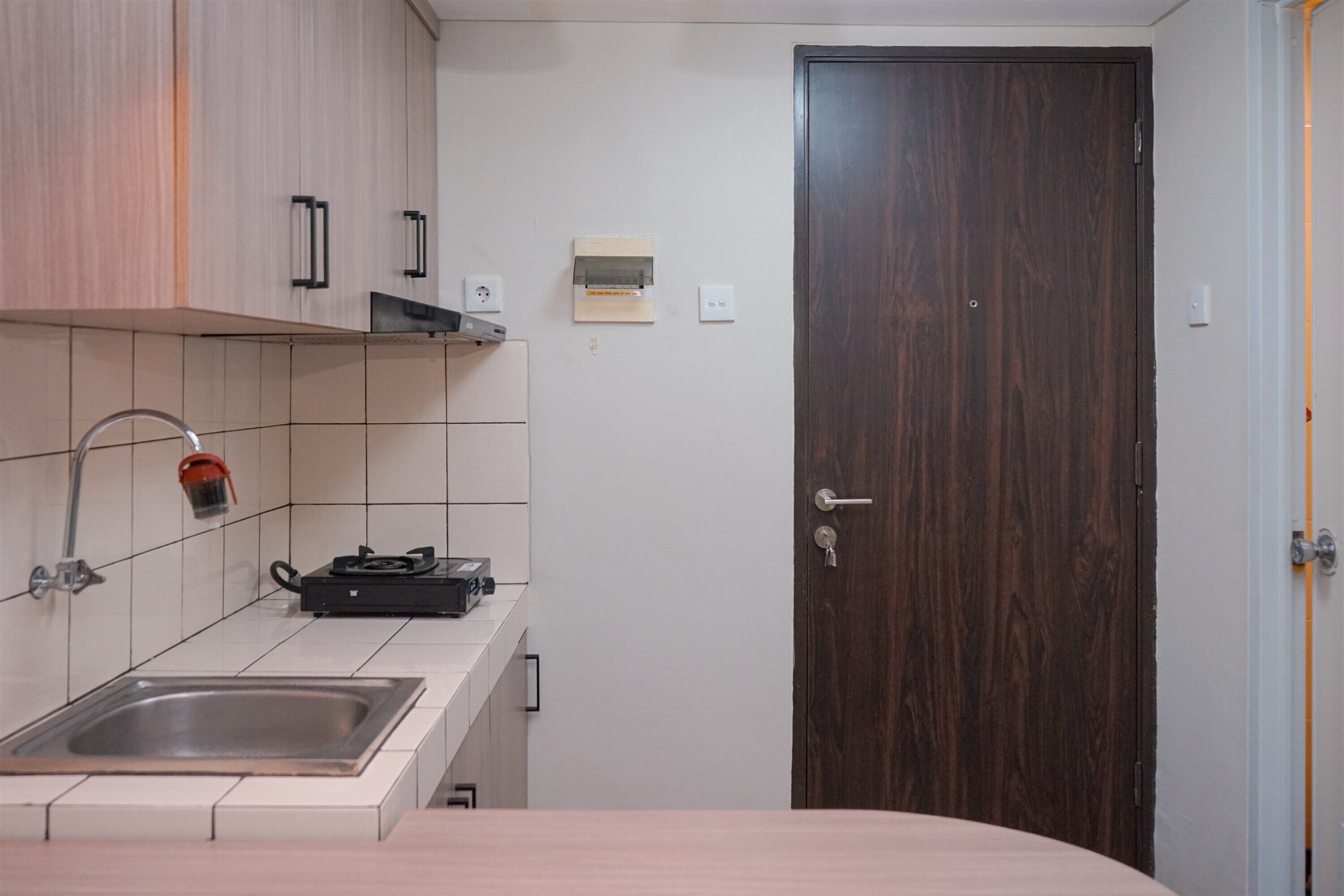 A compact kitchen with a sink, a stove, and a dark wooden door.