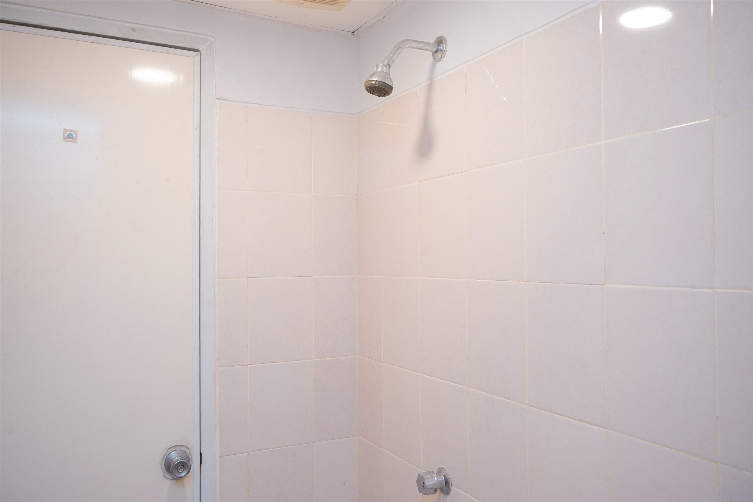 Un baño con azulejos blancos, un cabezal de ducha y una puerta.