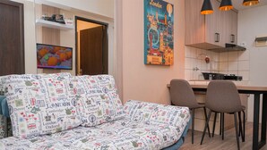 A modern living room with a patterned sofa, a television, and a kitchen area with a dining table and chairs. - Good Place and Homey 2BR at Apartment Serpong Greenview (South Tangerang)