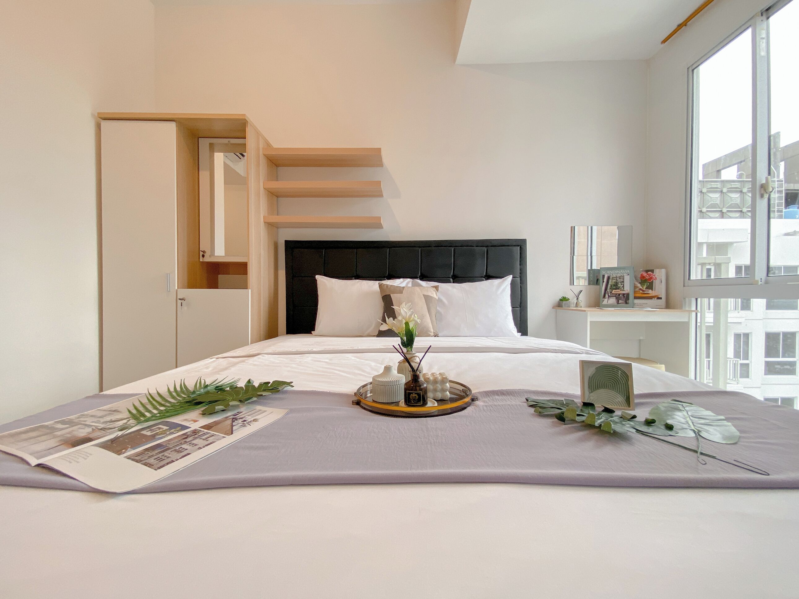 A modern bedroom with a large bed, a headboard, a bedside table, and a window.