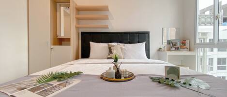 A modern bedroom with a large bed, a headboard, a bedside table, and a window.