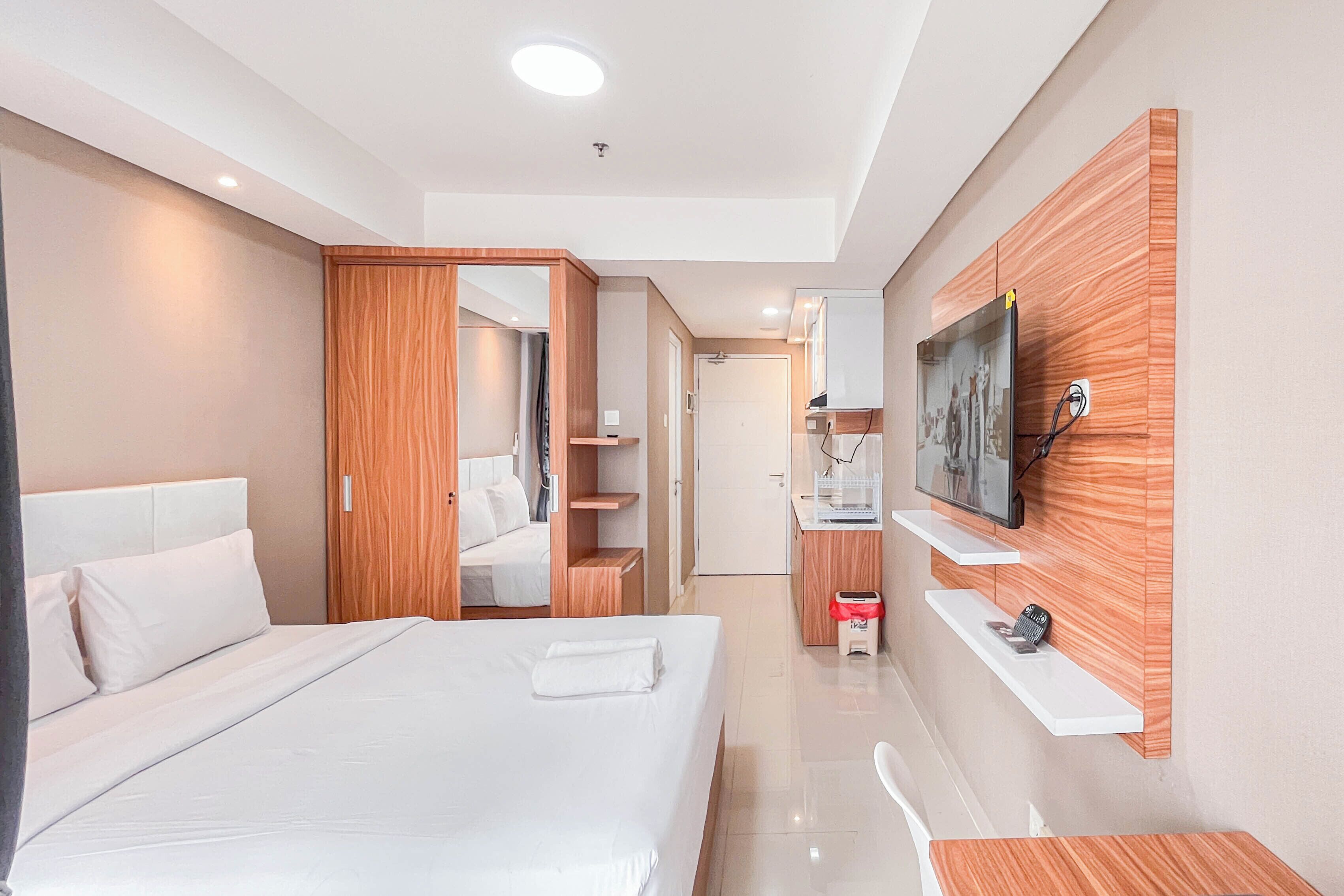 A modern hotel room with a bed, wooden wardrobe, a TV mounted on the wall, and a small desk with a chair.