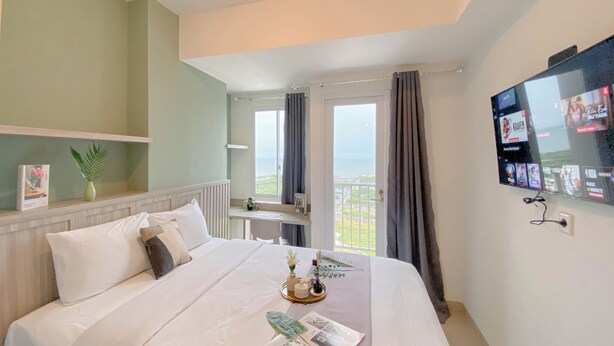 Ein Hotelzimmer mit Bett, Schreibtisch, Fernseher und einem Balkon mit Vorhängen.