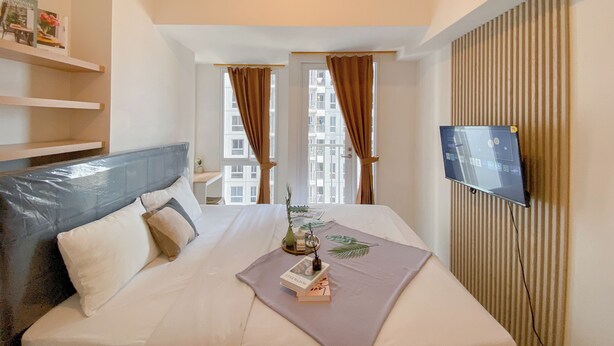 Una habitación de hotel con una cama, un televisor en la pared y una ventana con cortinas.