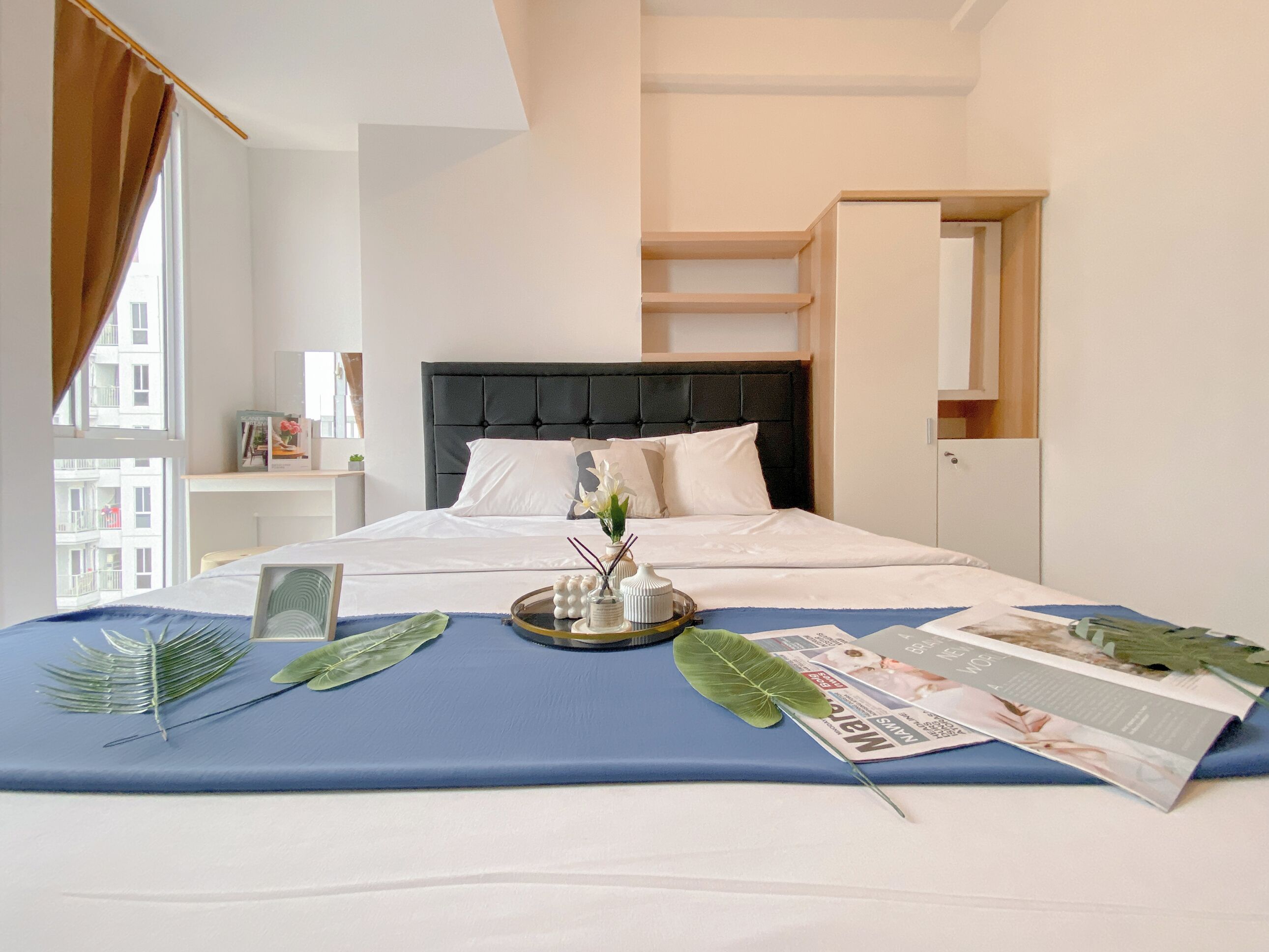 A neatly made bed with a blue bedspread, a tray with decorative items, and a magazine.