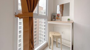 A small bathroom with a window, a stool, a mirror, and a shelf with a book and a plant. - Best Furnished and Homey Studio at Tokyo Riverside PIK 2 Apartment (Teluknaga)