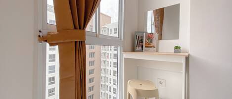 A small bathroom with a window, a stool, a mirror, and a shelf with a book and a plant.