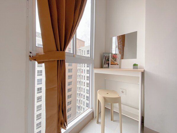 A small bathroom with a window, a stool, a mirror, and a shelf with a book and a plant. - Beautiful and Homey Studio Apartment at Tokyo Riverside PIK 2 (Teluknaga)