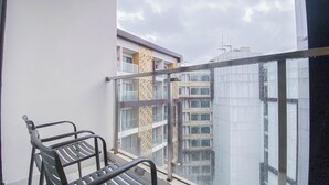 A balcony with two metal chairs, a glass railing, and a view of a building with multiple windows and balconies. - Good and Comfy Studio at Patraland Amarta Apartment (Ngaglik)