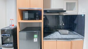 A compact kitchenette with a microwave, refrigerator, and sink. - Good and Comfy Studio at Patraland Amarta Apartment (Ngaglik)