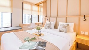 A modern hotel room with a large bed, bedside tables, a small seating area, and large windows.