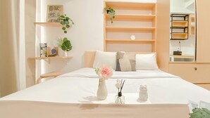 Ein ordentlich eingerichtetes Hotelzimmer mit einem großen Bett, einem Nachttisch mit Blumenvase sowie einem Regal mit Büchern und Pflanzen.