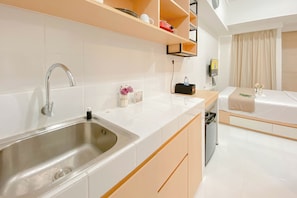 A modern hotel room with a kitchen area, including a sink, countertop, and wooden cabinets. - Comfortable and Compact Studio Apartment Tokyo Riverside PIK 2 (Teluknaga)