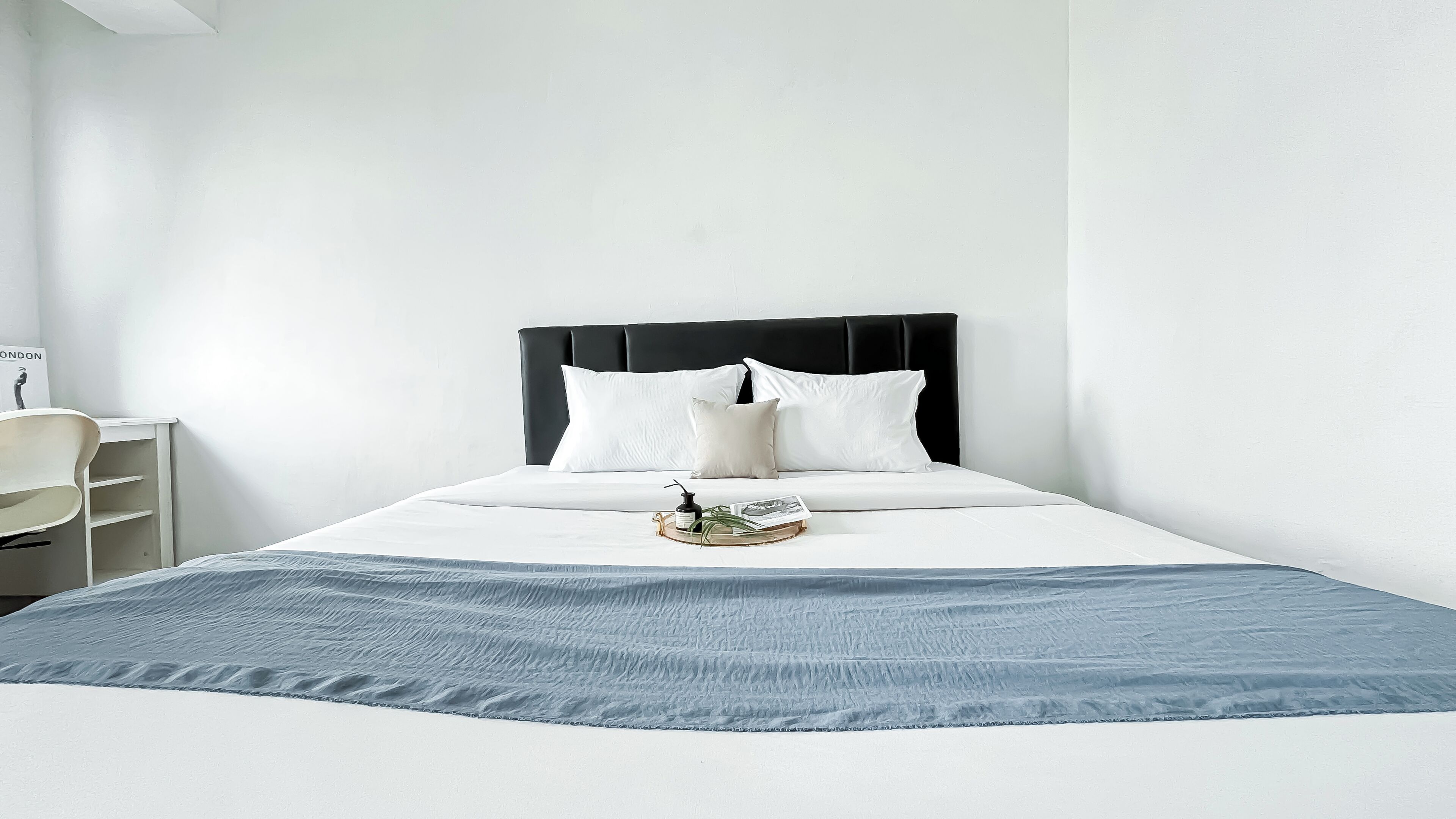 A neatly made bed with a black headboard, white bedding, and a tray with a bottle and a book.