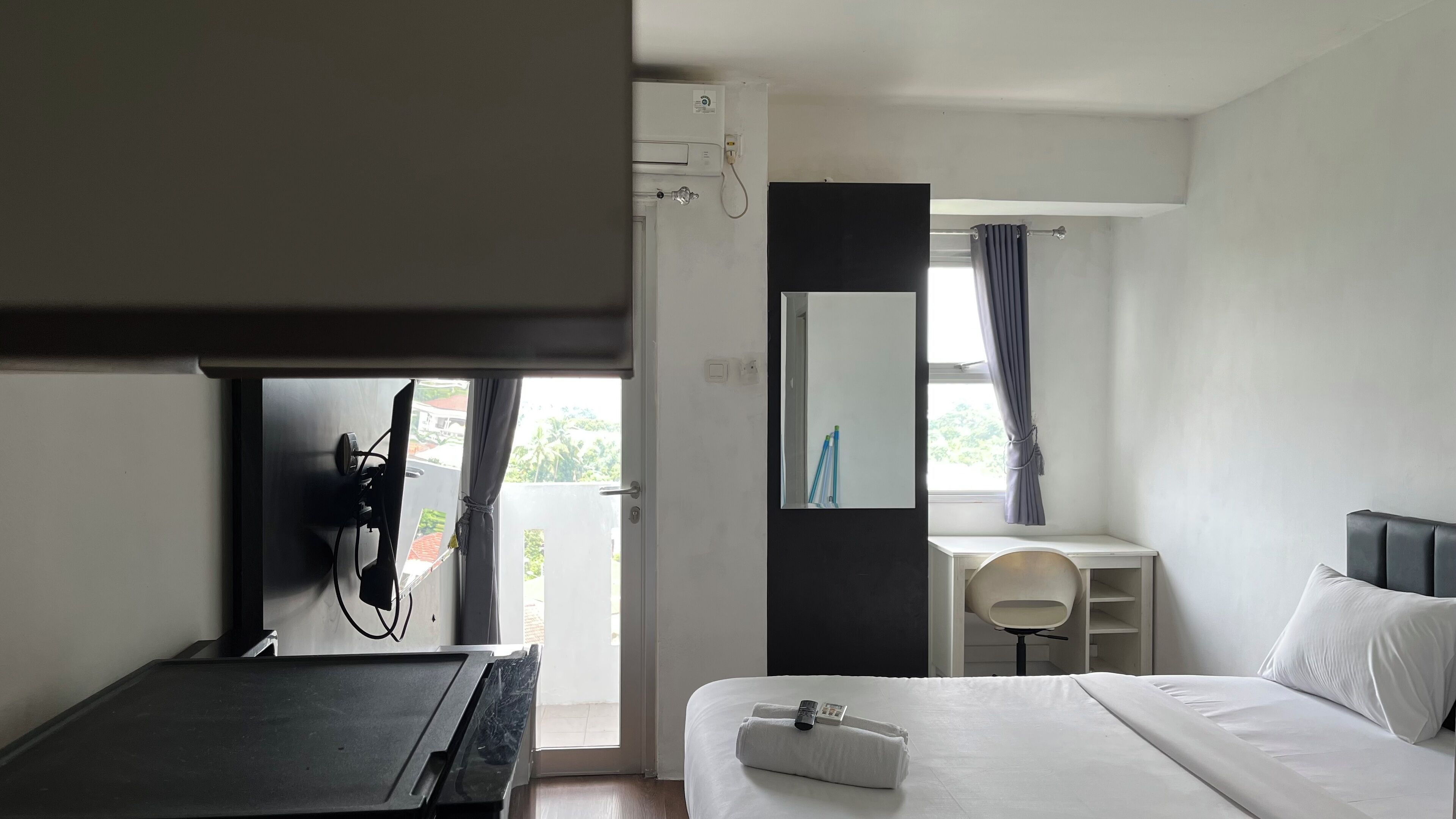 A hotel room with a bed, a desk, a chair, a mirror, and a window with curtains.