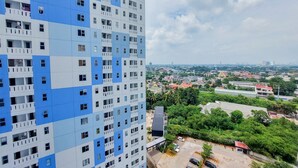 Un immeuble de grande hauteur à la façade bleue et blanche, doté de nombreux balcons et offrant une vue sur un paysage urbain, avec des espaces verts et d’autres bâtiments en arrière-plan.