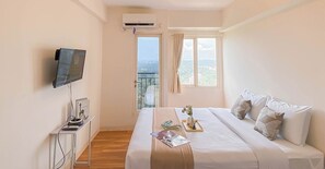 Habitación de hotel con cama, televisión, ventana con cortinas y vistas al balcón.