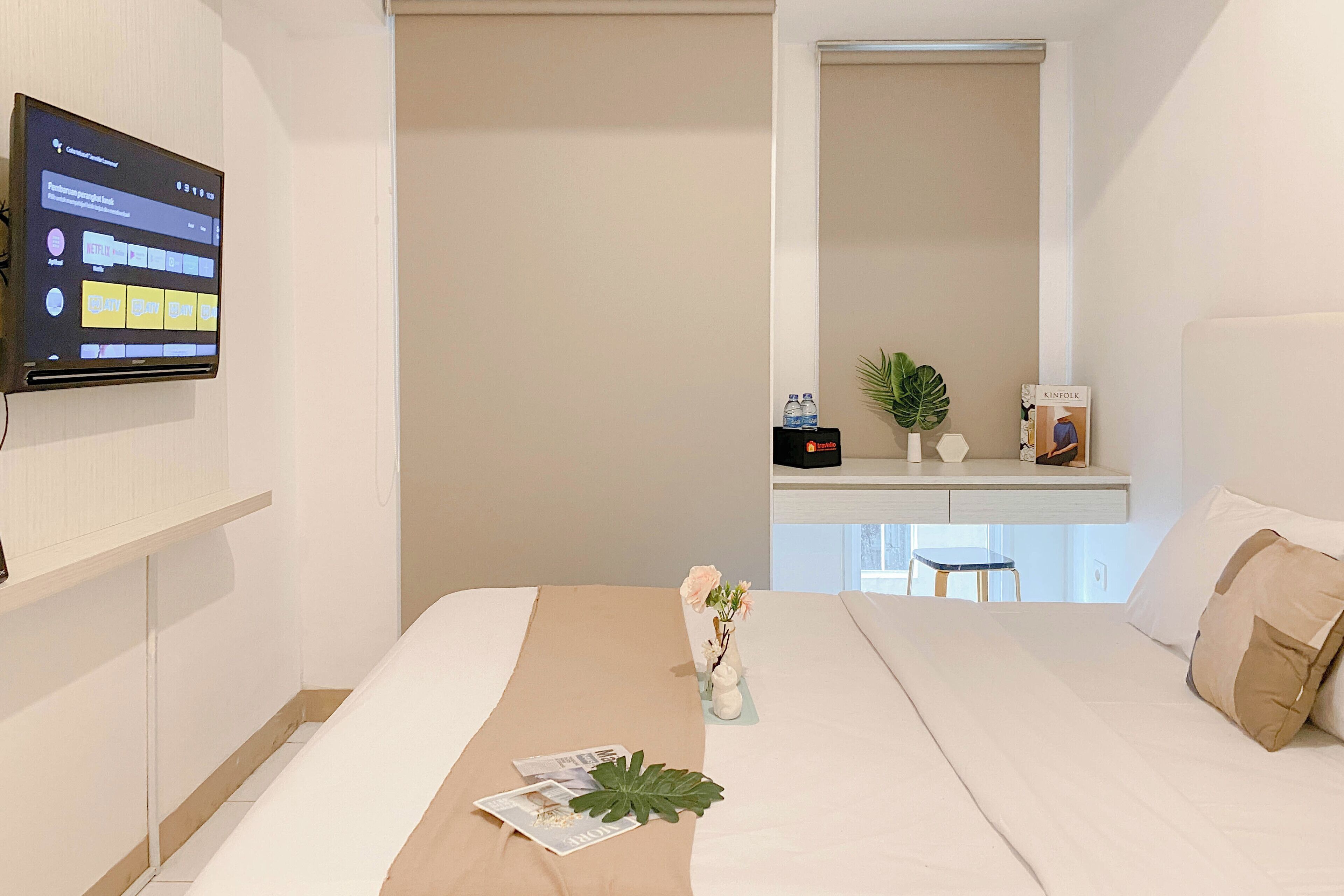 Una camera d'albergo con un letto, una televisione a schermo piatto fissata al muro, un tavolino con un vaso di fiori e una finestra vista esterna.