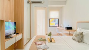 A hotel room with a bed, a desk, a TV, and an air conditioning unit. - Nice Studio Room Apartment Transpark Cibubur (Depok)