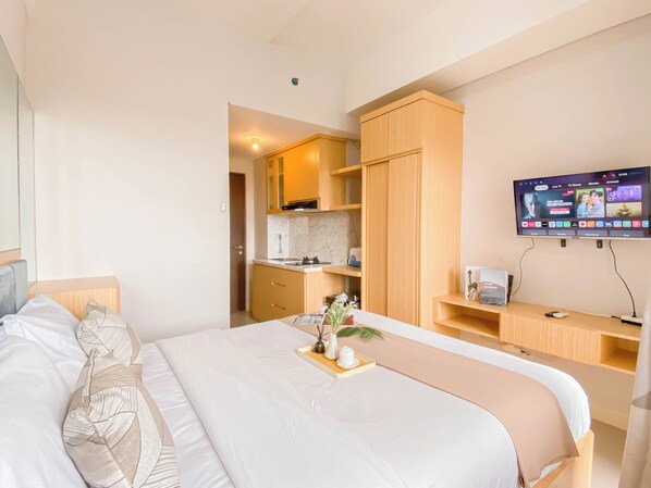 A hotel room with a bed, a desk, a TV, and a kitchenette.