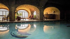 En indendørs swimmingpool med hvælvede murstenslofter, bænke og potteplanter.