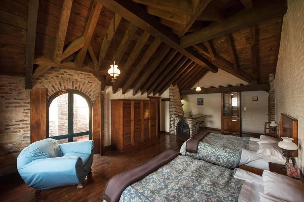 Una habitación rústica con vigas de madera, chimenea de piedra y un amplio ventanal de arco.