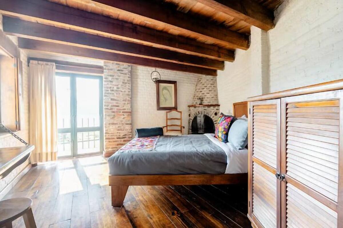 Un dormitorio con cama de madera, pared de piedra y un ventanal grande.